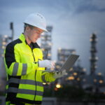 Worker in safety gear using laptop at industrial site during twilight reactive and predictive maintenance